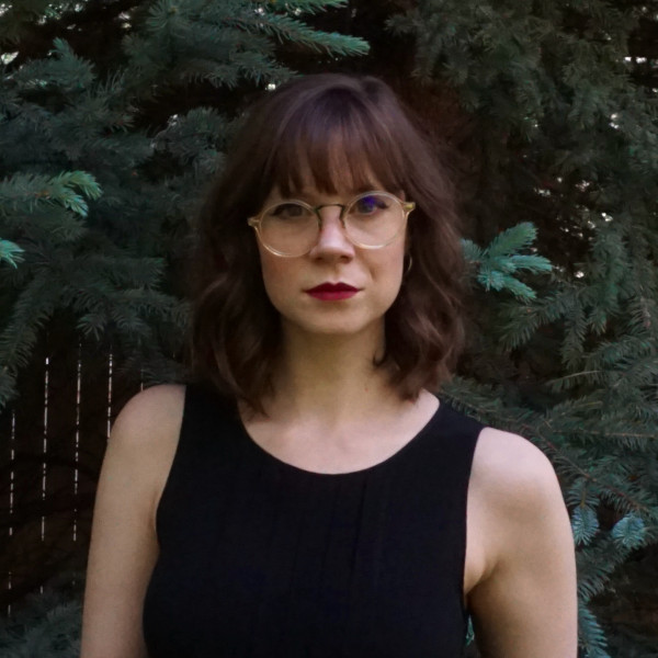 Profile image of the Writing Your Artist Statement instructor. She wears glasses and stands in front of a fir tree.