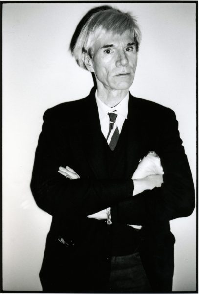 Black and White photo of Andy Warhol standing in a suit and tie